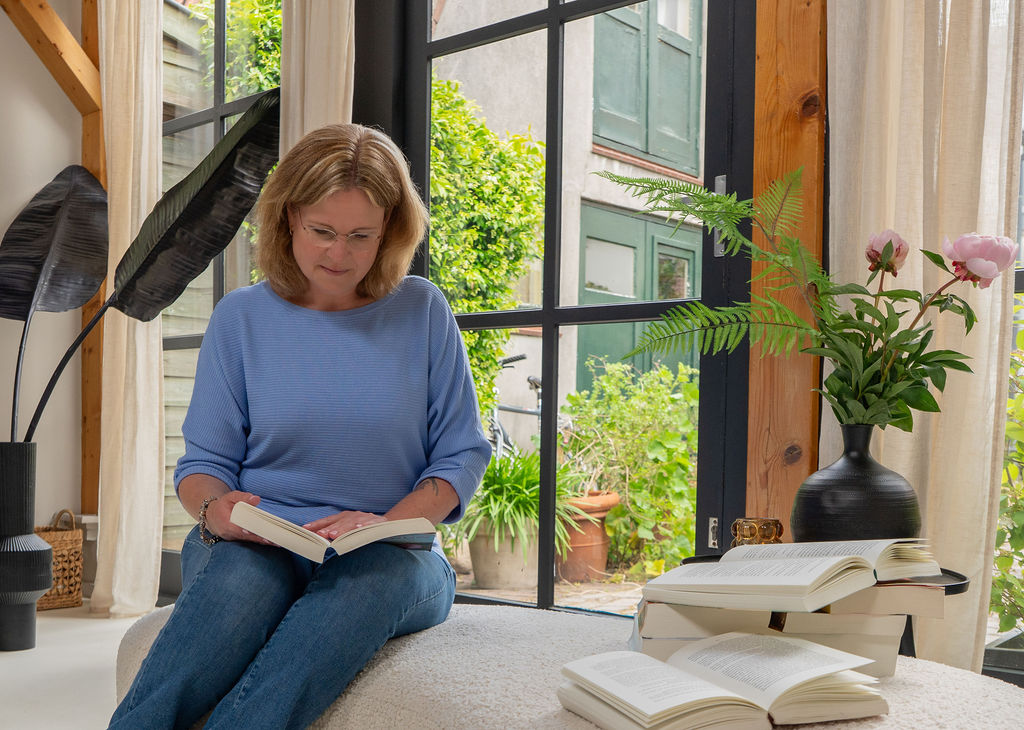Ghislaine Mulder leest een zelf uitgegeven boek buiten bij een raam met planten